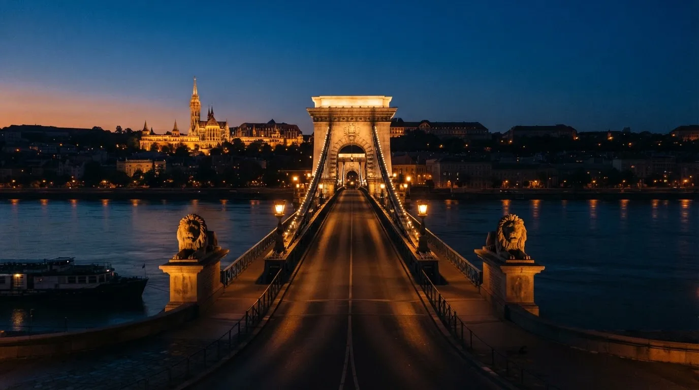 A budapesti Lánchíd esti fényekben a Duna fölött, a háttérben a budai Vár, forgalom nélküli rakpart.